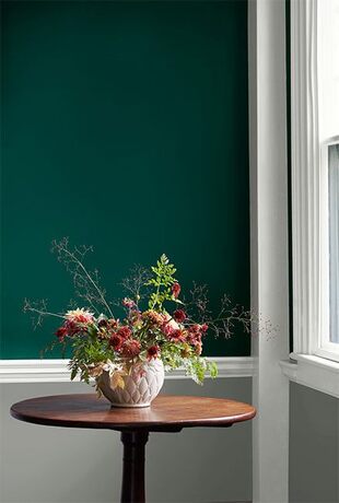 Una pared verde cazador con molduras blancas y revestimiento de madera gris enmarca una mesa redonda
